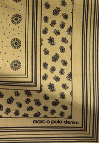 Żółta tkanina z czarnymi wzorami, w tym kropkami, kwiatami i motywami paisley. Posiada czarne obramowanie i zawiera tekst "marc o polo denim."