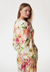 Bloemrijke jurk met grote roze, gele en groene bloemenprints. Lange, volumineuze mouwen en een aansluitend tailleontwerp creëren een gestructureerde silhoutte.