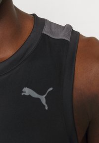 Débardeur de sport noir avec des accents gris sur les épaules et un logo réfléchissant subtil. Le matériau semble lisse et ajusté.