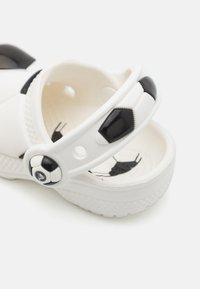 Sandal de plástico branco com um padrão de bola de futebol preto e detalhe na tira, apresentando uma sola texturizada e um acento de logótipo em círculo na lateral.