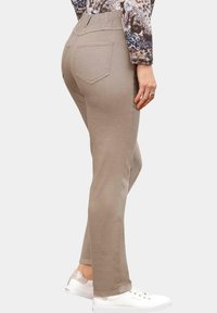 Pantalons stretch beiges avec une taille élastique et deux poches arrière, associés à des baskets blanches. Le tissu a une texture lisse.