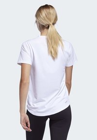 Hvid bomulds-T-shirt med løs pasform, korte ærmer og afrundet kant, kombineret med sorte leggings, set bagfra.