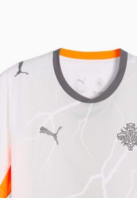 Maillot de sport Puma blanc avec col gris, motif d'éclair, logos Puma sur l'épaule et la poitrine, ainsi qu'un emblème géométrique sur le côté droit de la poitrine.
