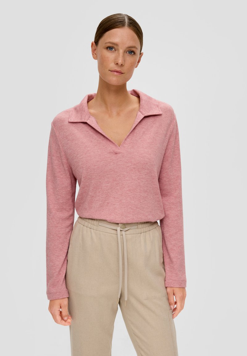 Różowy sweter z długim rękawem i dekoltem w kształcie litery V, z kołnierzykiem; wykonany z miękkiego materiału; zestawiony z jasnobeżowymi spodniami z elastycznym paskiem.