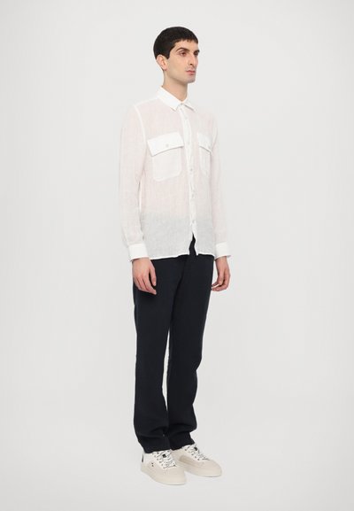 White, lightweight, long-sleeve shirt with two front pockets, button-down collar, and a slightly sheer texture, paired with dark pants and shoes.