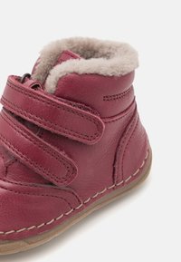 Stivale in pelle maroon per bambini con rivestimento in pile beige e due cinturini regolabili con chiusura a strappo, su uno sfondo bianco.