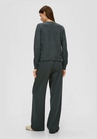 Grauer Strickpullover mit langen Ärmeln, kombiniert mit weit geschnittenen, dunkelgrauen Hosen. Der Stoff scheint weich zu sein, und die Hose hat Seitentaschen.