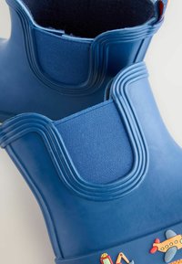 Blauwe rubberlaarzen met een textuur op de bovenkant, stoffen accenten en kleurrijke, speelse patronen aan de voorkant. Rond model en stevige constructie.