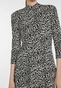 Sukienka z długim rękawem i wysokim kołnierzem, z czarno-kremowym abstrakcyjnym wzorem. Tkanina ma gładką teksturę i dopasowany krój.