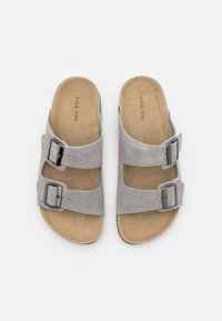 Sandales en velours gris à enfiler avec deux sangles adjustables dotées de boucles métalliques. Semelle intérieure beige rembourrée et semelle en caoutchouc plate.