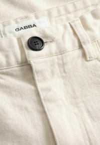 Tuva pieglausta krēmkrāsas biksu josta ar melnu pogu un iekšā izšūtu "GABBA" zīmola etiķeti.