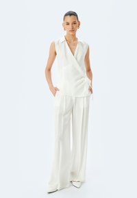 Witte mouwloze omslagtop met een V-hals, geknoopt in de taille, gecombineerd met een broek met wijde pijpen. Soepele, lichte stof met een subtiele glans.