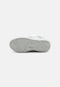 Hvit sneakers med en teksturert gummiyttersåle som har et sikksakkmønster og Fila-logo. Designet inkluderer snøring og en glatt syntetisk overdel.