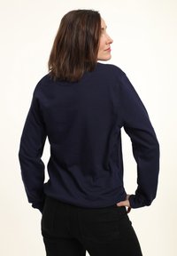 Marineblauer Pullover mit langen Ärmeln, Rundhalsausschnitt und weicher Textur. Auffällige Details sind der lässige Schnitt und das schlichte Design ohne Logos.