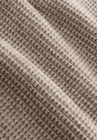 Close-up of beige waffle-knit fabric showing textured, grid-like pattern with soft folds and shadows.