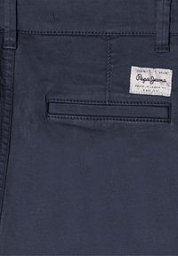 Temno modri denim hlače z zadnjim žepom z woveno nalepko, podrobnostmi šivanja in gladko teksturo. Okrašene z blagovno znamko.
