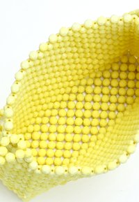Cestino giallo realizzato con perline testurizzate. Forma arrotondata con un motivo esagonale e una finitura liscia. Design con apertura superiore per un accesso facile.