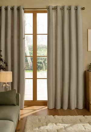 Geschlossene beige Vorhänge hängen an einer goldenen Gardinenstange und bedecken eine Holztür mit Glasrahmen, durch die draußen Grün zu sehen ist.