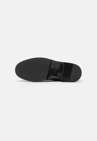 Semelle de chaussure en cuir noir avec une finition lisse, un motif de grip texturé et un petit talon. Pas de marquage ni d'éléments décoratifs visibles.