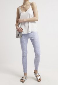 Top blanco sin mangas, ligero, leggings lavanda con estampado y sandalias metálicas plateadas; incluye un pequeño bolso cruzado gris.