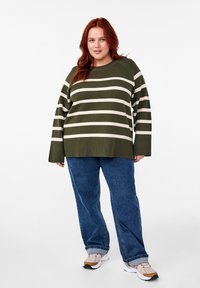 Maglione a righe verde e crema con una vestibilità morbida, maniche lunghe e orlo a costine, abbinato a jeans in denim blu chiaro e sneakers.