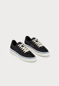 Black canvas sneakers with cream laces and blue accents. White rubber sole with stitching details and a streamlined design.