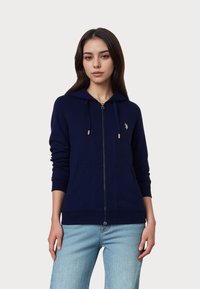 Tengerészkék zipzáras kapucnis pulóver puha anyagból, elülső zsebbel, húzózsinóros kapucnival és arany színű fém kiegészítőkkel. Diszkrét logó a mellkason.
