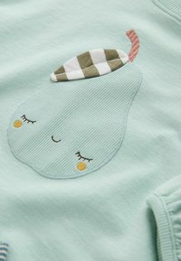 Tissu vert clair avec un motif de poire endormie cousu, présentant des yeux fermés, des joues orange, une feuille à carreaux et une tige marron.