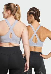 Light gray sports bras with cross-back straps, featuring a cut-out design. Black leggings with varied textures and logo accents.
