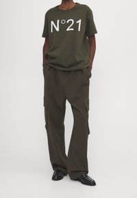 Camiseta de algodón verde oliva con estampado blanco "N°21", combinada con pantalones cargo a juego que cuentan con bolsillos laterales y un corte relajado. Zapatos negros.