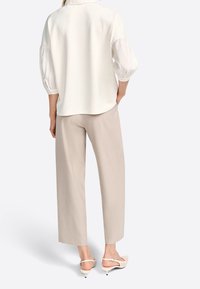 Weißes Blusenshirt mit puffartigen Ärmeln, kombiniert mit beigen weit geschnittenen Hosen und hellen High Heels. Glatte Textur und minimalistisches Design.