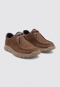Chaussures en cuir marron avec une forme arrondie, présentant des coutures apparentes, des lacets décoratifs et une semelle en caoutchouc beige flexible.