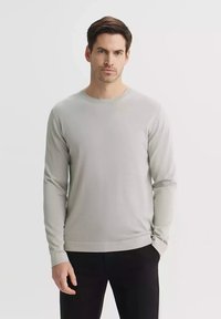 Jasnoszary sweter z długim rękawem wykonany z miękkiego materiału, z okrągłym dekoltem, ściągaczami przy mankietach i dopasowanym krojem, w połączeniu z czarnymi spodniami.