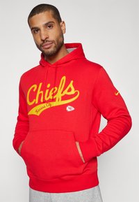 Raudona gobtuvinė megztinė su geltonai išsiuvinėtais žodžiais "Chiefs" ir "Kansas City". Turi priekinę kišenę ir Nike logotipą ant rankovės. Pagaminta iš medvilnės mišinio.