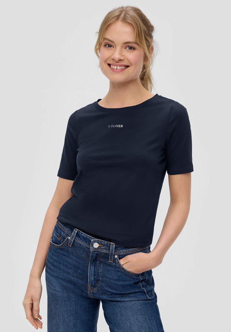 Navyblauwe t-shirt met korte mouwen van zachte katoen, met een ronde hals en witte logo-details aan de voorkant. Gecombineerd met denim jeans.