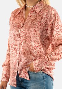Camisa de patrón rosa y roja con diseño de botones, mangas largas y cuello. Hecha de una tela liviana con un acabado texturizado.
