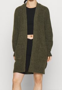 Olivgrön stickad cardigan med öppen front, långa ärmar och två framfickor. Mjuk textur med en avslappnad passform och längd till mitten av låret.