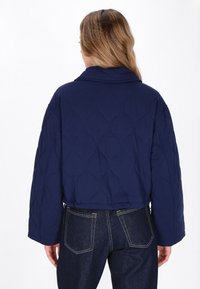 Marineblå cropped quiltet jakke med en stor krave og et struktureret bølgemønster. Den har brede ærmer og en afslappet pasform.