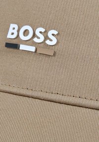 Cappellino da baseball beige in tessuto testurizzato. Presenta un logo bianco "BOSS" e tre accenti colorati: nero, bianco e marrone chiaro.