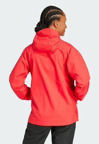 Red waterproof jacket with a hood, featuring long sleeves and a relaxed fit. Smooth texture with minimalistic design, suitable for outdoor use.
