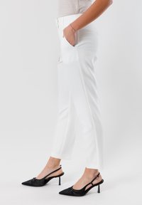 Pantaloni bianchi su misura con una texture liscia e tasche laterali, abbinati a tacchi a punta neri con design slingback.