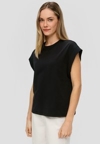 Zwart katoenen T-shirt met korte opgerolde mouwen, ronde hals, relaxte pasvorm en gladde structuur. G gedragen met lichte broek.