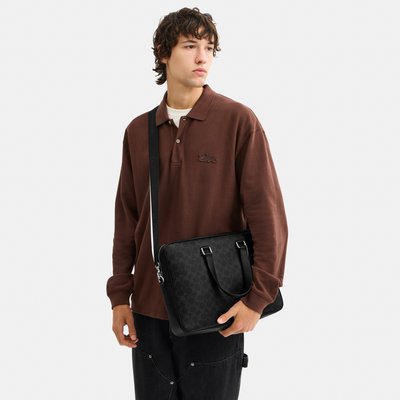 Jeune homme aux cheveux bruns courts portant un polo marron à manches longues et un pantalon noir, tenant un sac à épaule noir à motifs.