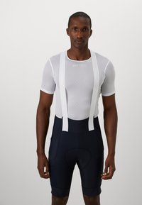 Ensemble de cyclisme pour hommes comprenant un maillot blanc à manches courtes en mesh et un cuissard bleu marine ajusté avec des bretelles blanches et un rembourrage au niveau du siège.
