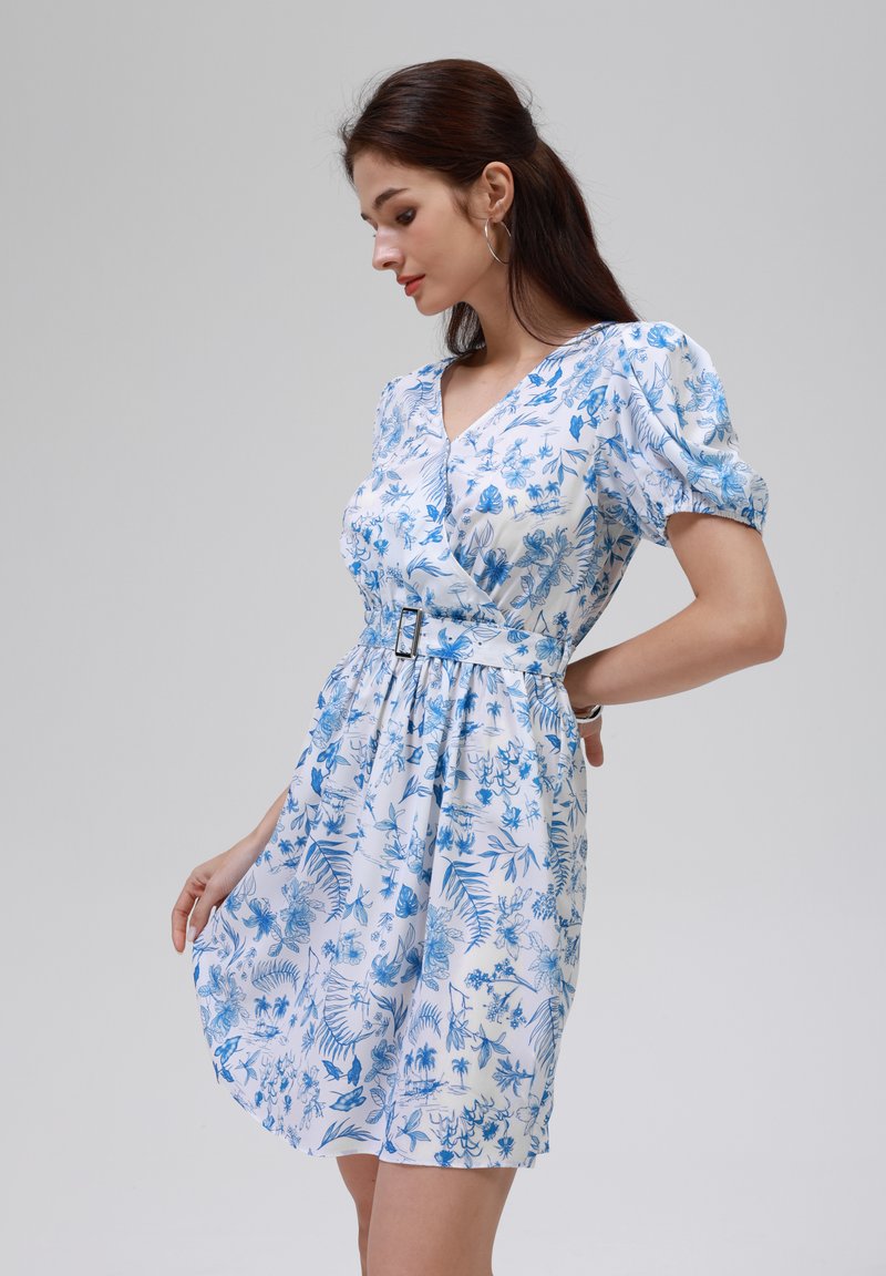 Robe blanche avec un motif floral bleu, décolleté en V, manches courtes bouffantes, taille cintrée avec une ceinture, et jupe A-line fluide, tissu lisse.
