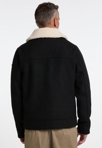Black wool-blend jacket featuring a cream, shearling collar, structured shape, and subtle seam detailing. No visible fastenings or accents.