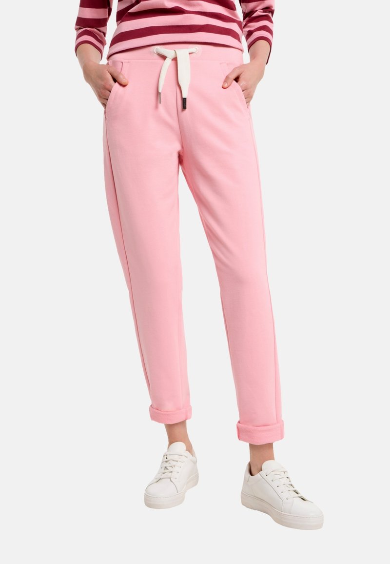 Light pink sweatpants with rolled cuffs, drawstring waist, two side pockets, and a soft texture. Paired with white sneakers.