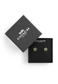 Gold-tone circular cufflinks with green enamel center featuring a "C" logo, presented in a black textured box with white branding.