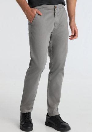 Chino gris avec une coupe ajustée, poches avant et fermeture à bouton. Il présente un tissu lisse et texturé, associé à des baskets noires.