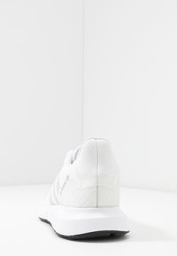 Witte sportieve schoen met een gestructureerde mesh bovenkant, een gevoerde kraag en een lichte zool met een zwarte buitenzool. Subtiel logo-detail aan de zijkant.